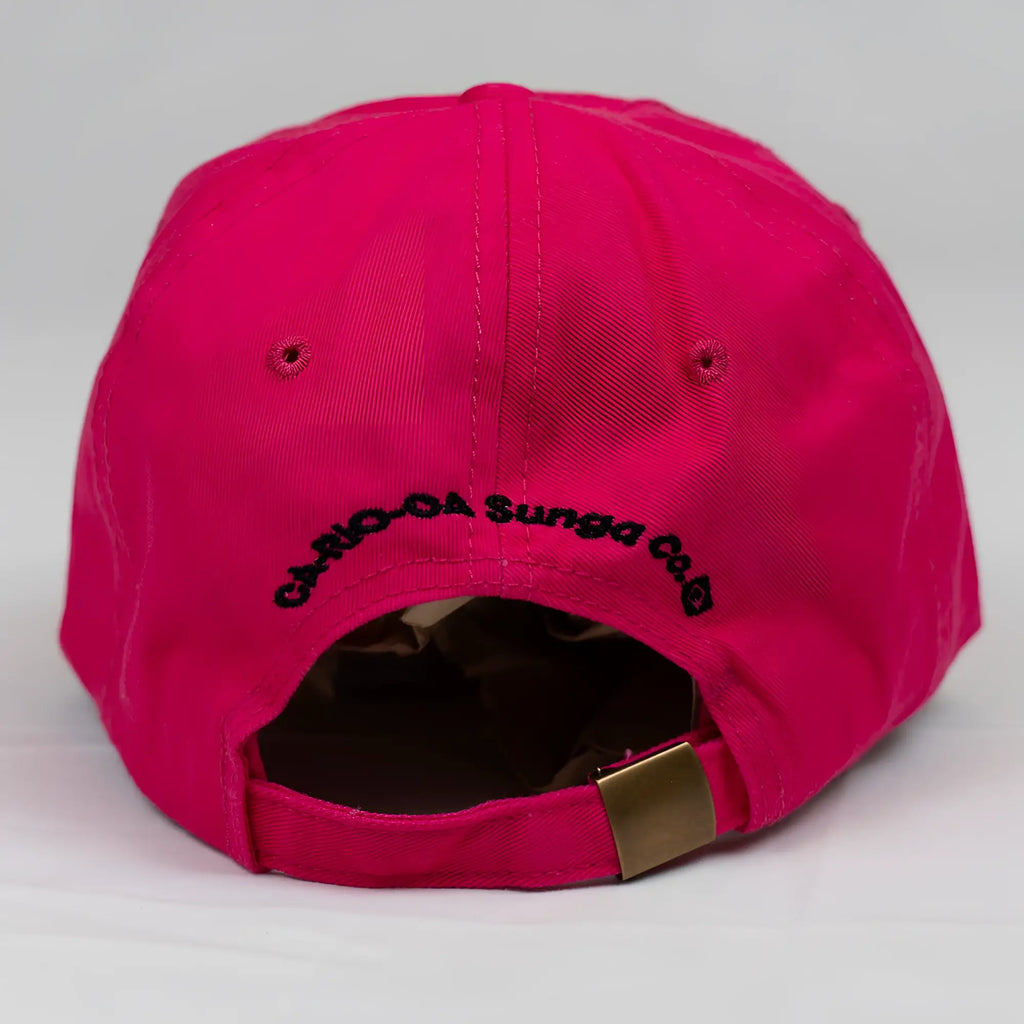 The back side of a vibrant fuchsia ca-rio-ca crest logo embroidered designer dad hat with black text and gold-tone strap