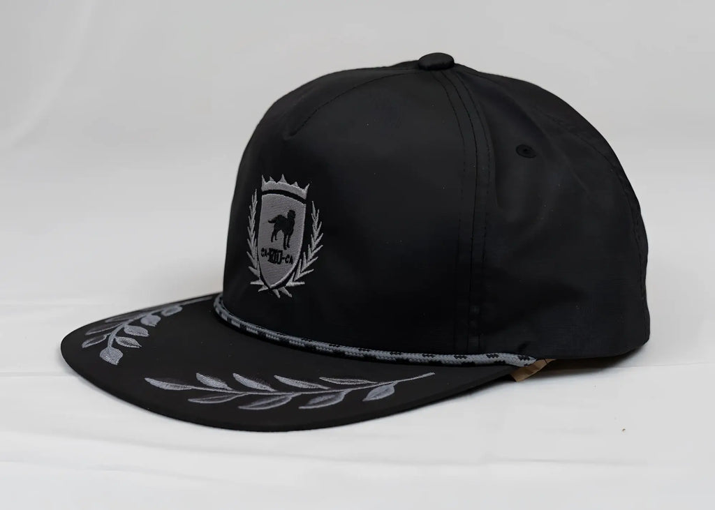 Black snapback cap with silver embroidered CA-RIO-CA crest logo and bay leaf pattern on the brim