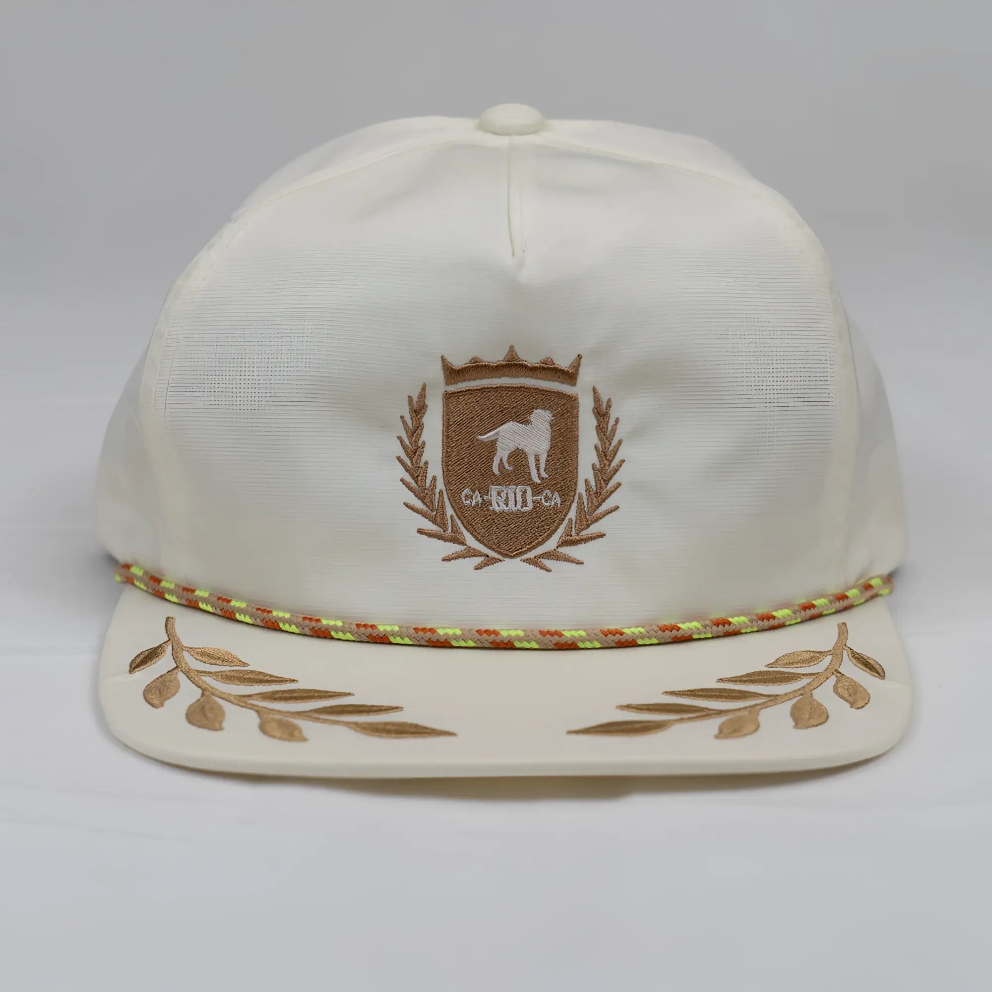 Cream-colored unstructured bay leaf snapback hat with brown dog crest embroidery and multicolored braided trim