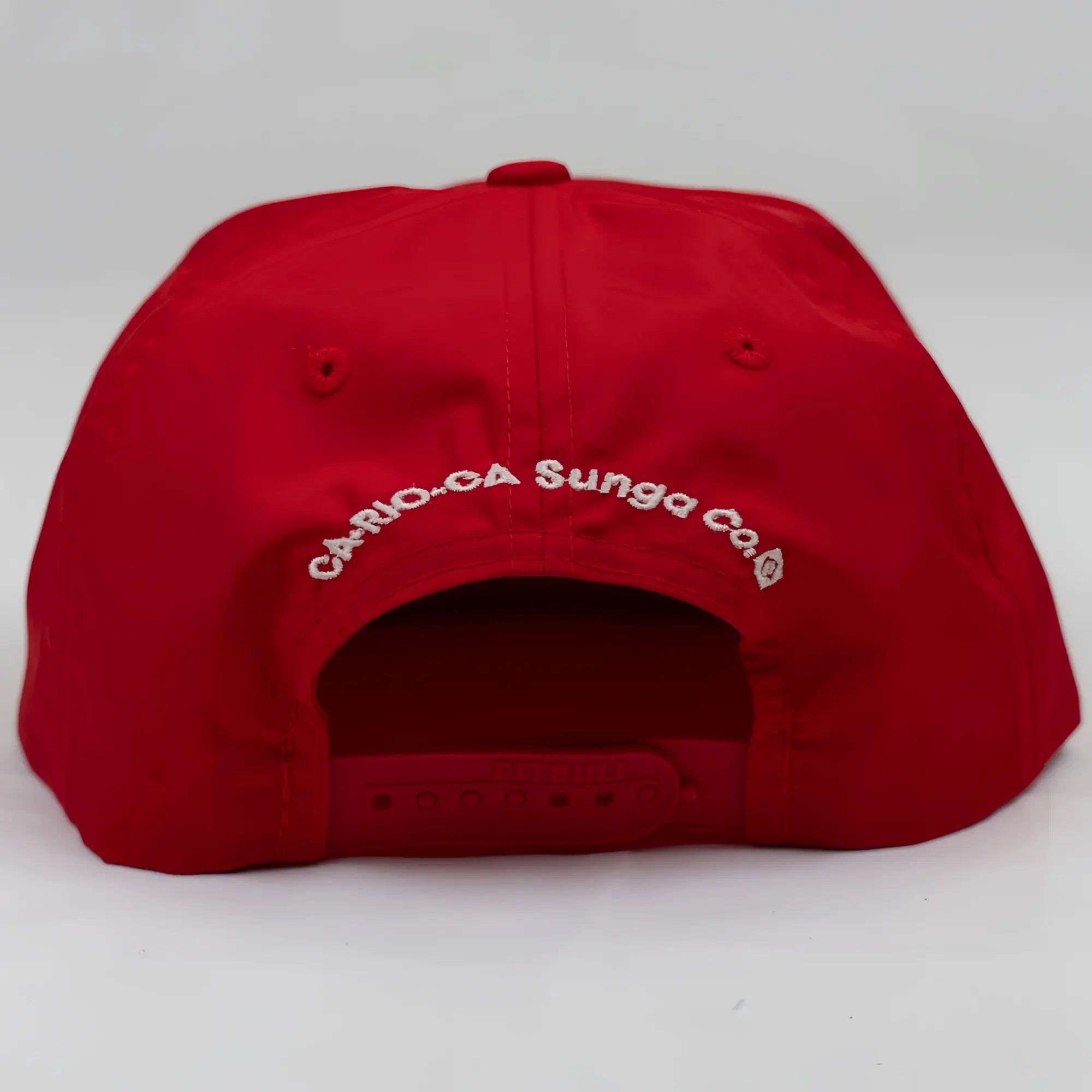 The back side of a vibrant red unstructured bay leaf snapback rope hat with white embroidered ca-rio-ca crest logo