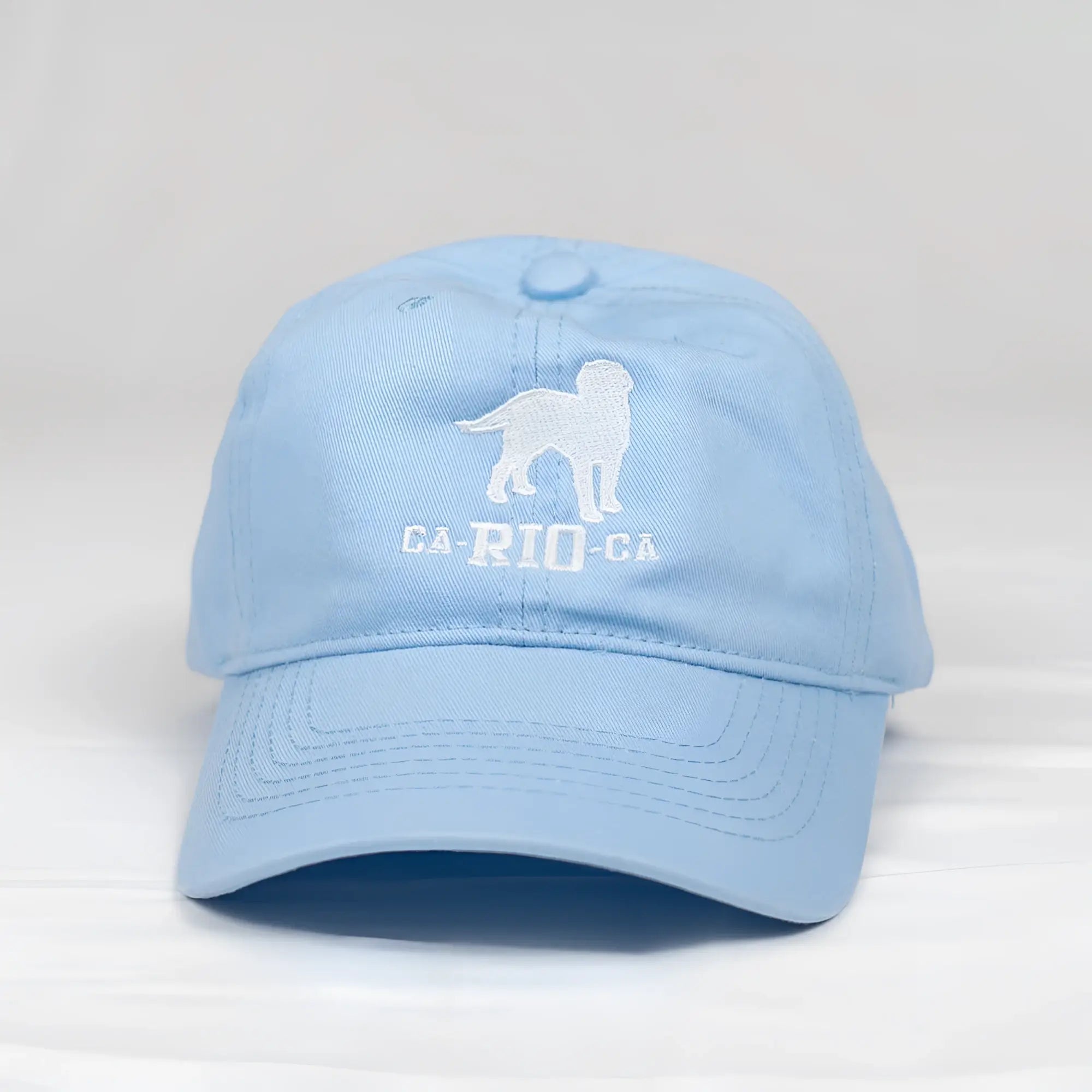 Light blue cotton baseball cap with white embroidered dog silhouette and ca-rio-ca text on the front panel