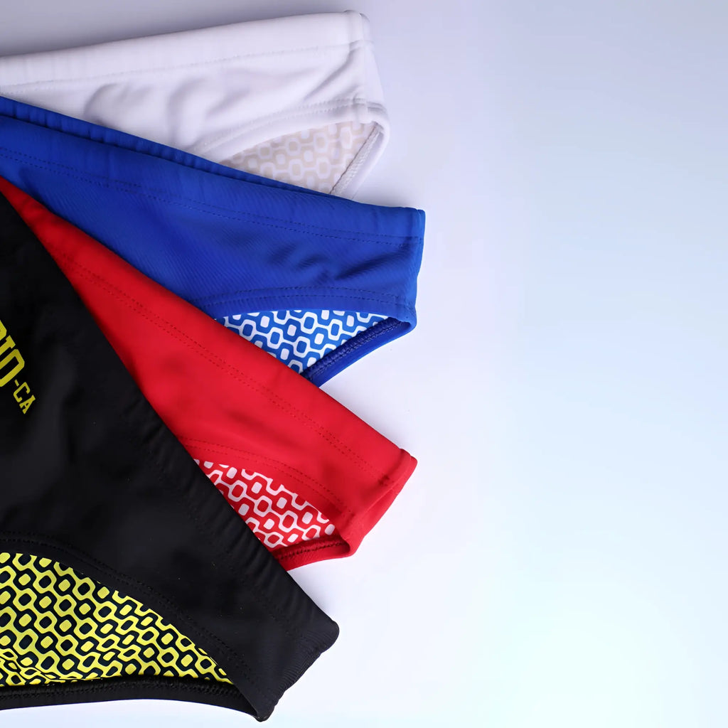 A stack of ca-rio-ca logo swim bikini athletic briefs in white blue red and black with patterned inner linings for men