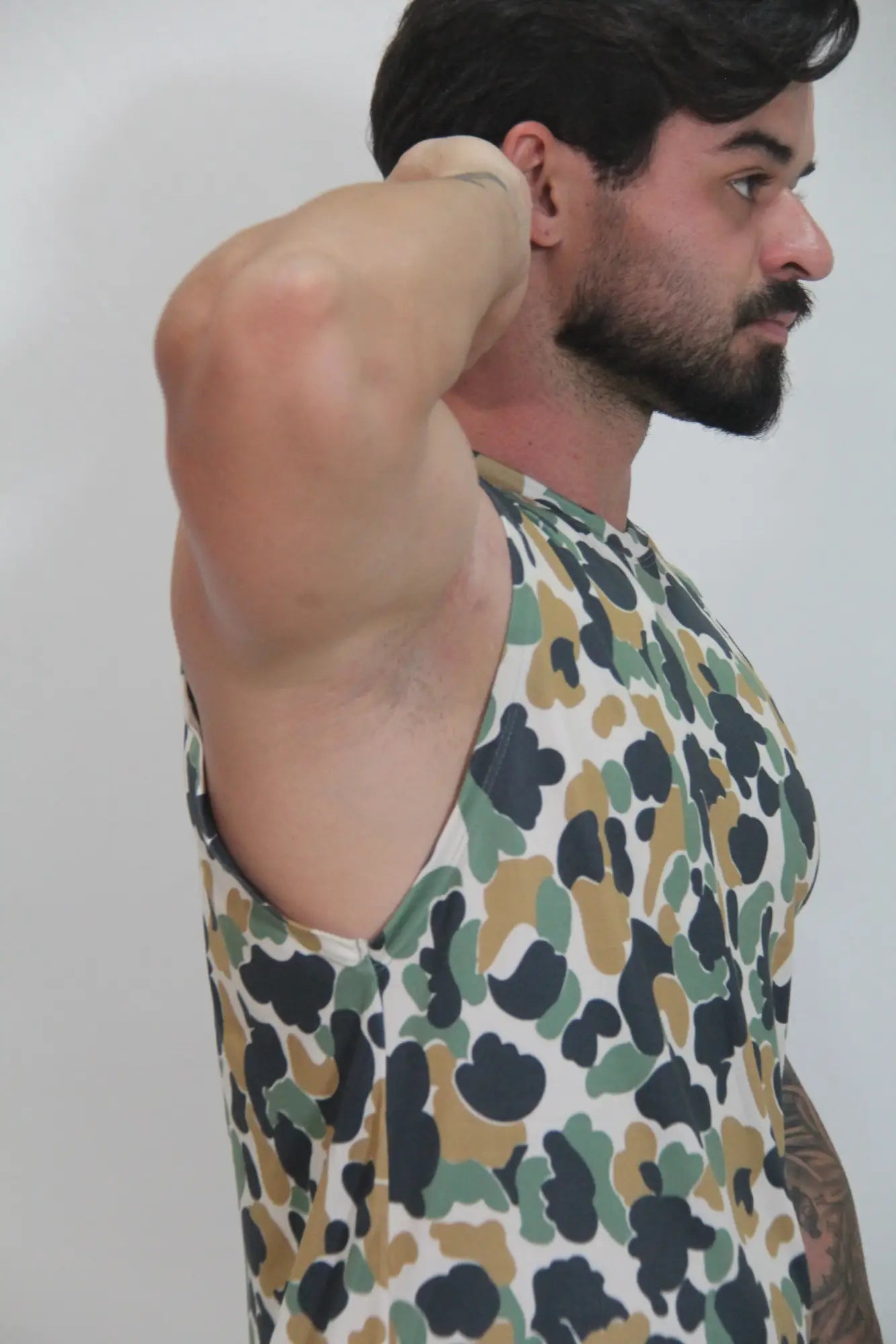 A man wearing a camouflage open arm tank top with black green and tan splotches on a white base