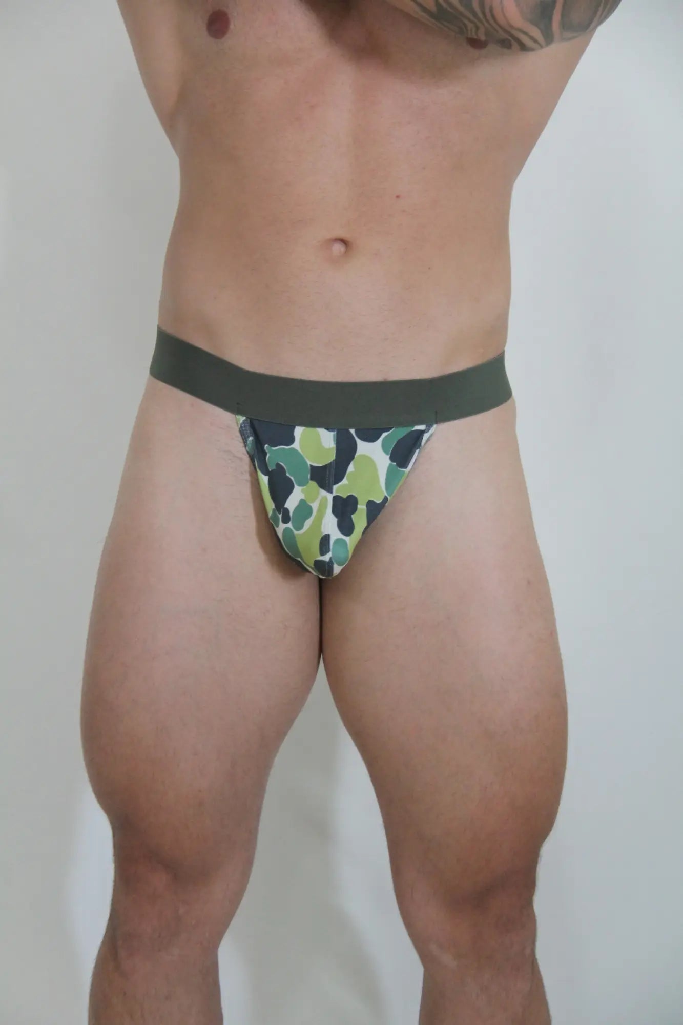 Camouflage thong briefs with green and black pattern and solid dark green waistband shown from the back side