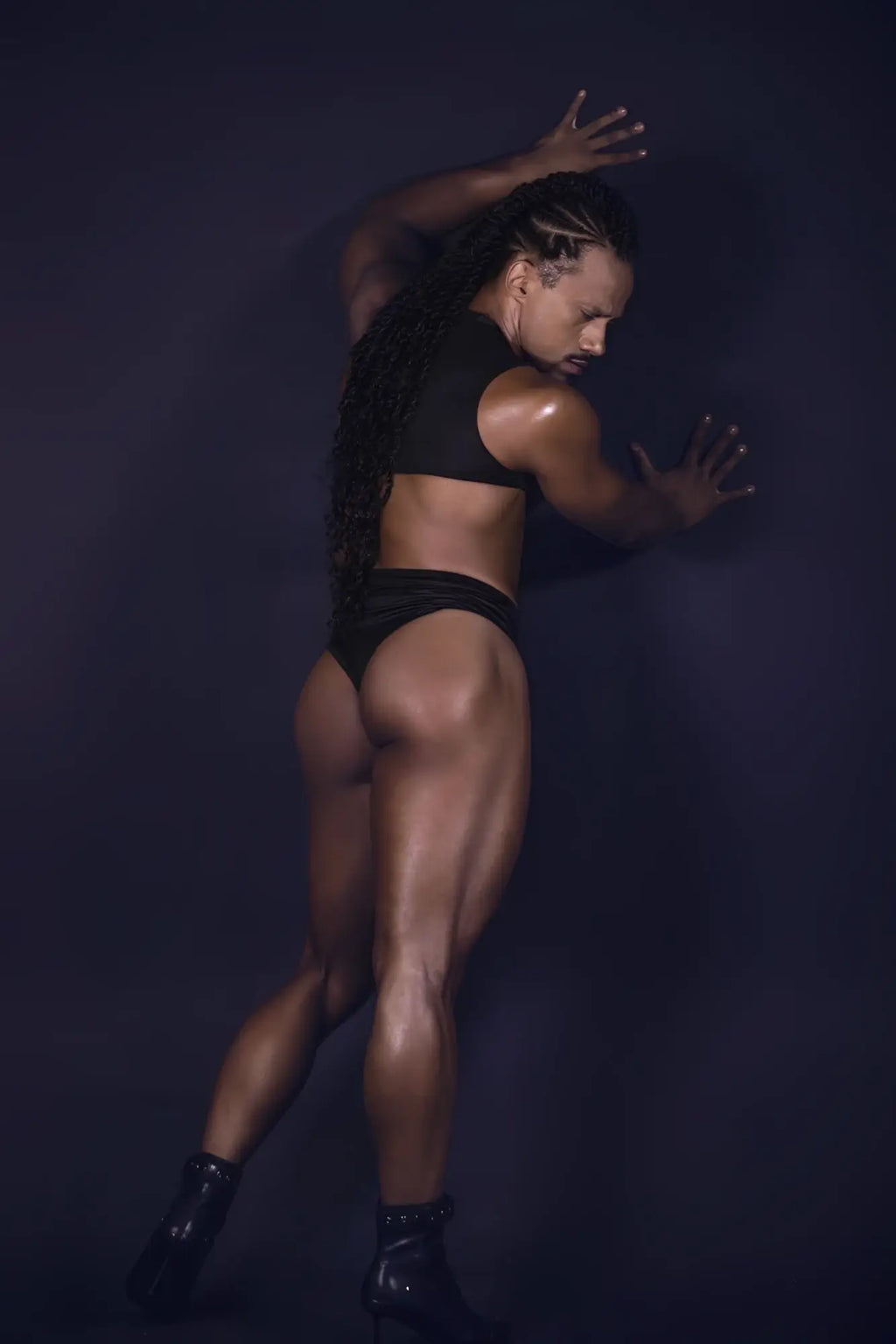 A muscular individual wearing a black candyMan 99783 one shoulder bodysuit with glossy black heeled boots