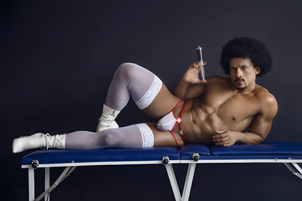 A muscular man with an afro lies on a blue table wearing candyMan 99833 murse thongs red-white with white lace stockings