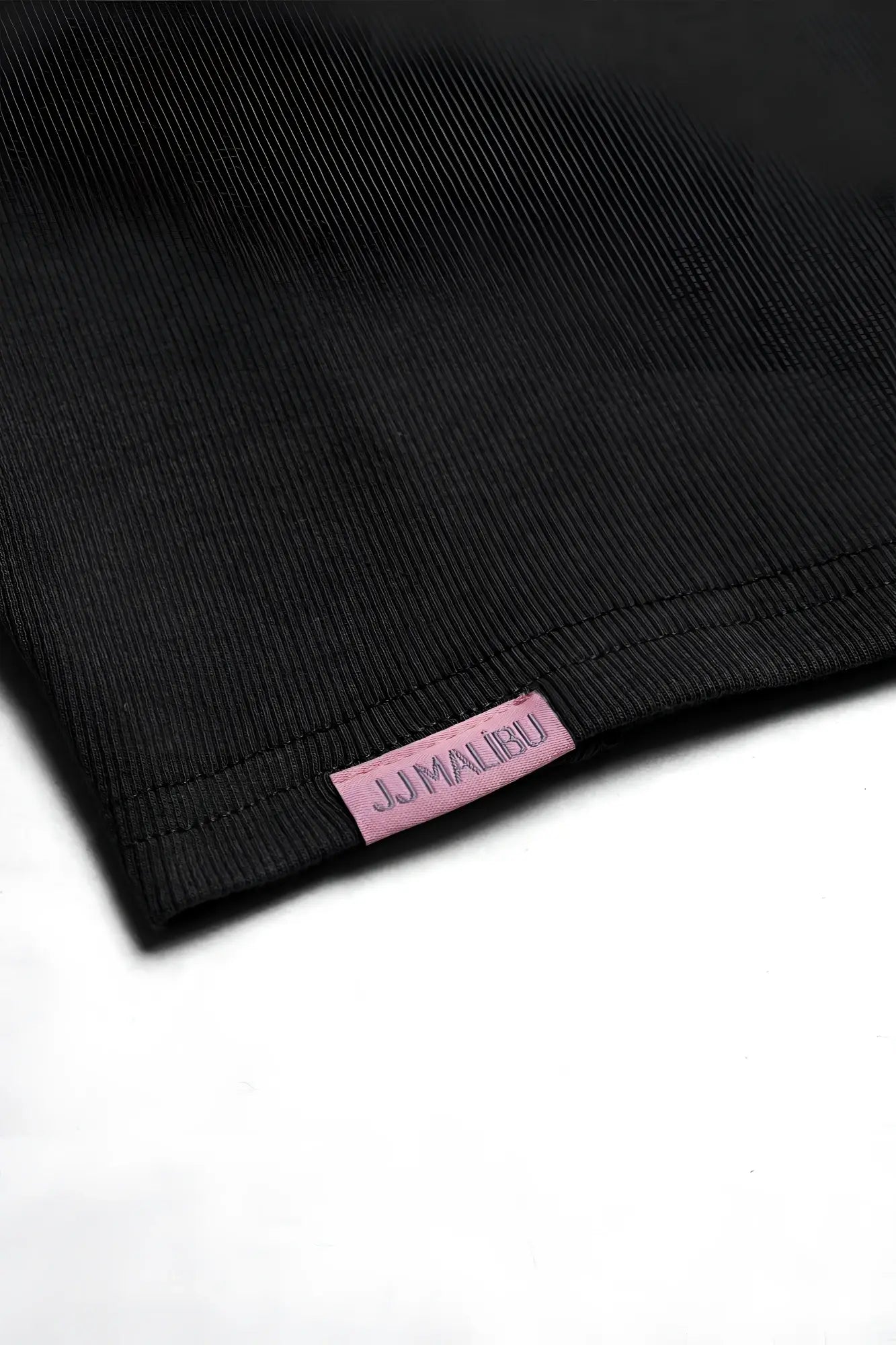 Black ribbed cotton cap sleeve crop top with pink jjmalibu brand tag visible in close-up view