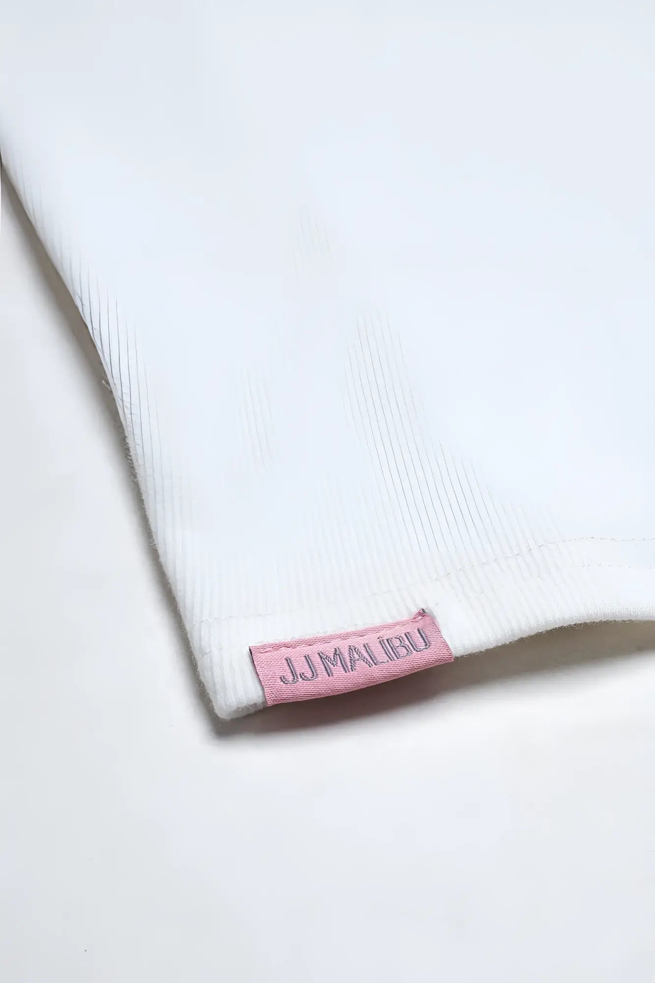 A soft white ribbed fabric cap sleeve rib knit crop top in ivory with a small pink jjmalibu woven label