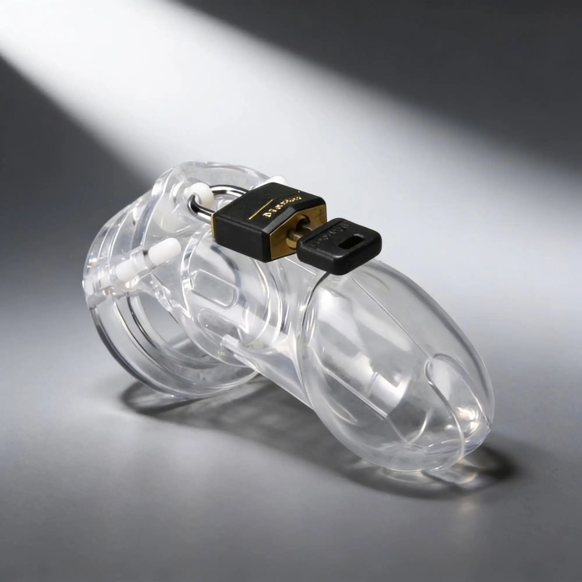 Clear CB-X CB6000 male chastity device with a base ring and cage, secured by a black and gold padlock with a key.