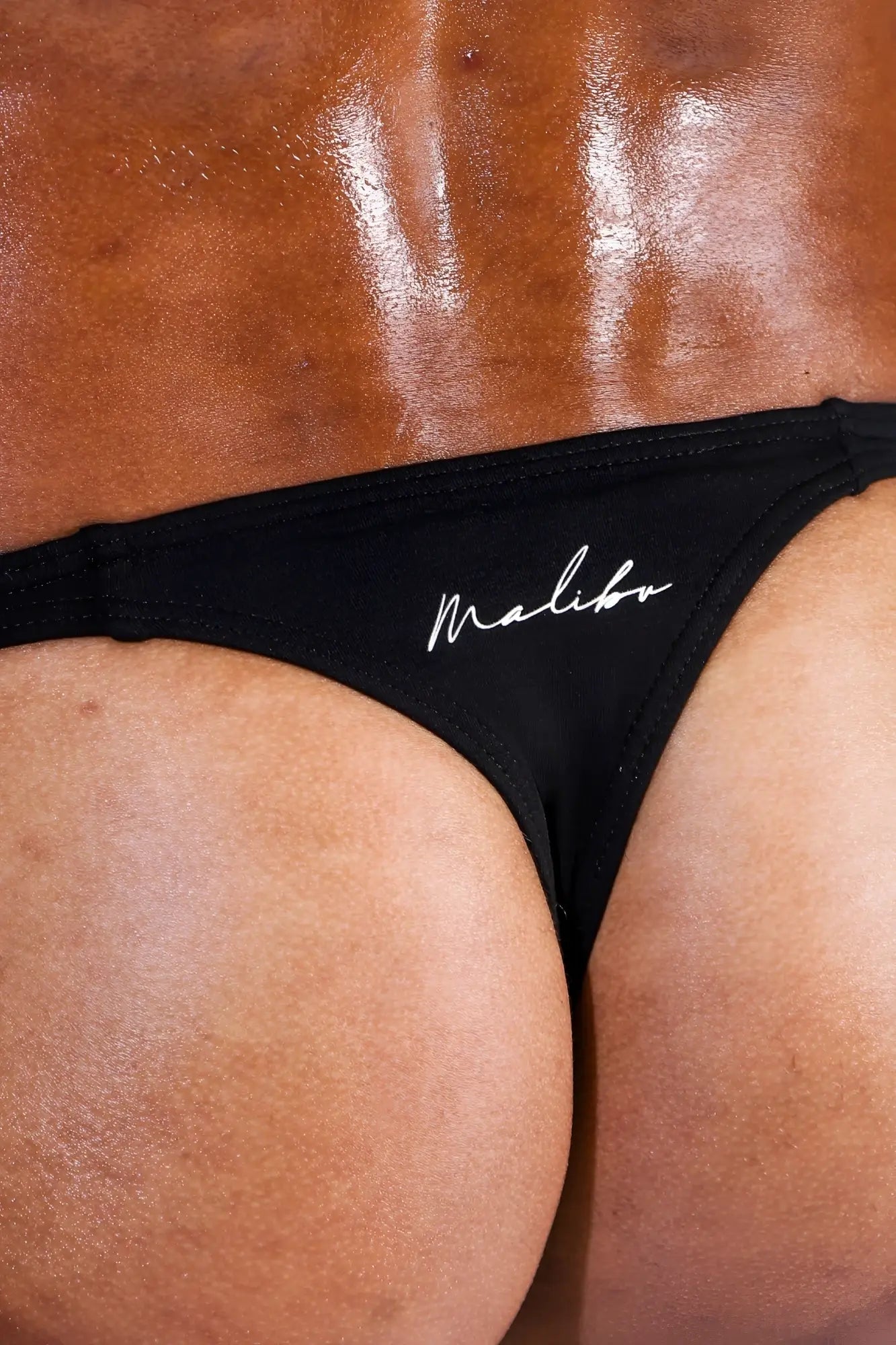 Black cheeky classic g-string thong with white cursive branding showing the front side in soft fabric