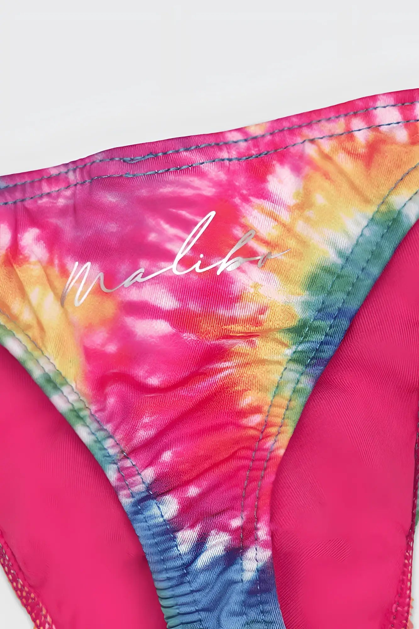 A vibrant rainbow tie dye cheeky classic g-string thong bikini bottom with a silver malibu logo on the back side