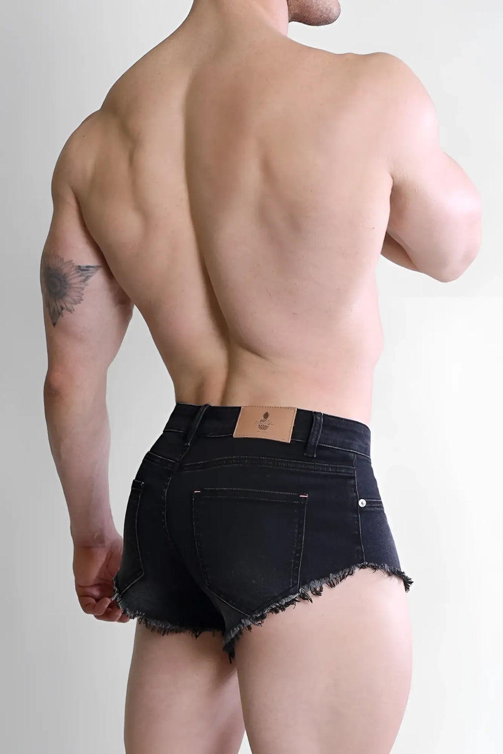 Black denim cheeky summer 2.5 inch brief shorts with frayed hem and brown leather brand patch on waistband