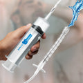 CleanStream 150 mL syringe with flexible attachment, showing water spraying from the nozzle. Handheld medical style.