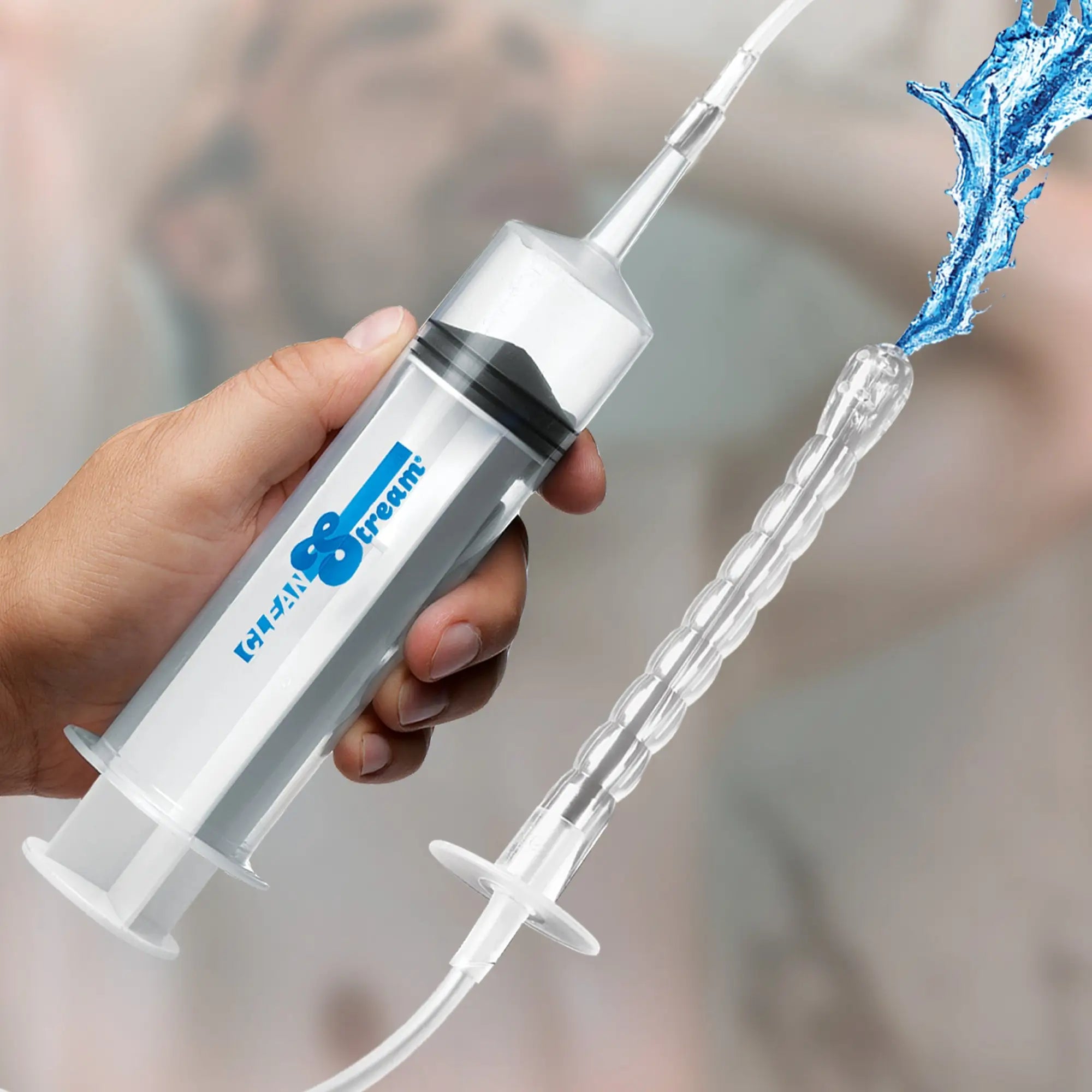 CleanStream 150 mL syringe with flexible attachment, showing water spraying from the nozzle. Handheld medical style.