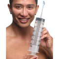 A smiling man holds a large, clear 300ml CleanStream enema syringe, with water spraying from the nozzle.