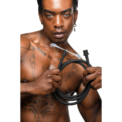 A tattooed man holds a coiled, black CleanStream Premium Silicone Enema Hose with water spraying from the nozzle.