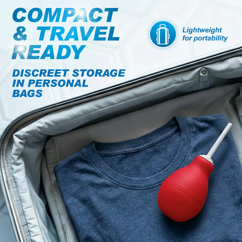 CleanStream red enema bulb with a white nozzle placed on a folded blue shirt inside a travel suitcase.