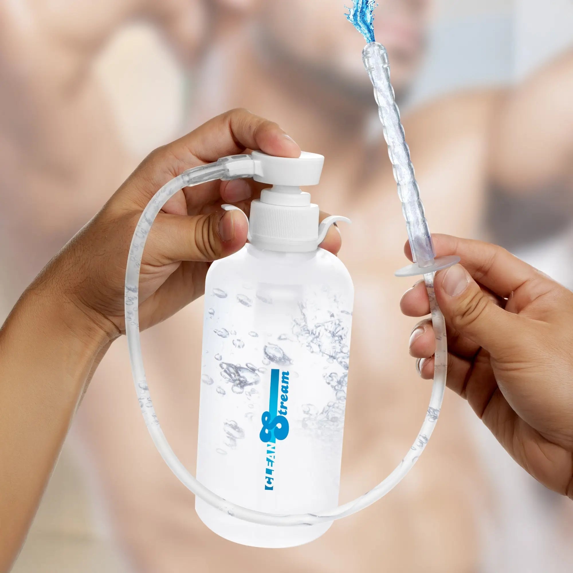 CleanStream XL clear enema bottle with pump, tubing, and ribbed nozzle spraying water. Hands holding device.