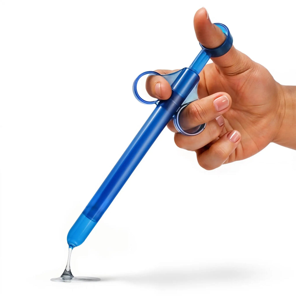 A hand holds the CleanStream XL Lubricant Launcher - CleanStream Blue, dispensing a small amount of clear enema lubricant onto a surface.