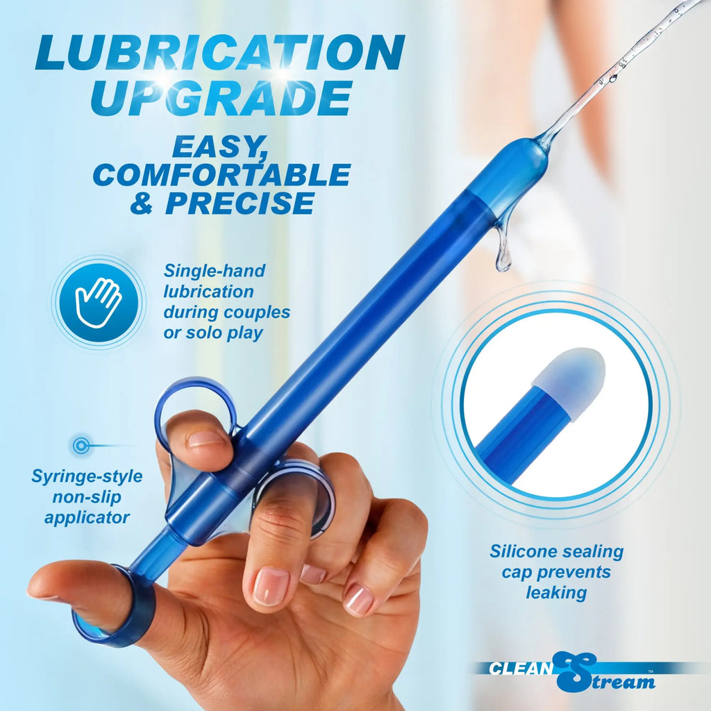 A hand grips the CleanStream XL Lubricant Launcher - CleanStream Blue, a blue syringe-style anal lube applicator. Water drips from its tip. Text notes its easy, precise use, single-hand grip, non-slip design, and silicone cap to prevent leaks.