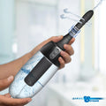CleanStream XL black automatic enema bulb with spinning tip, spraying water, held in hand against a blurred background.
