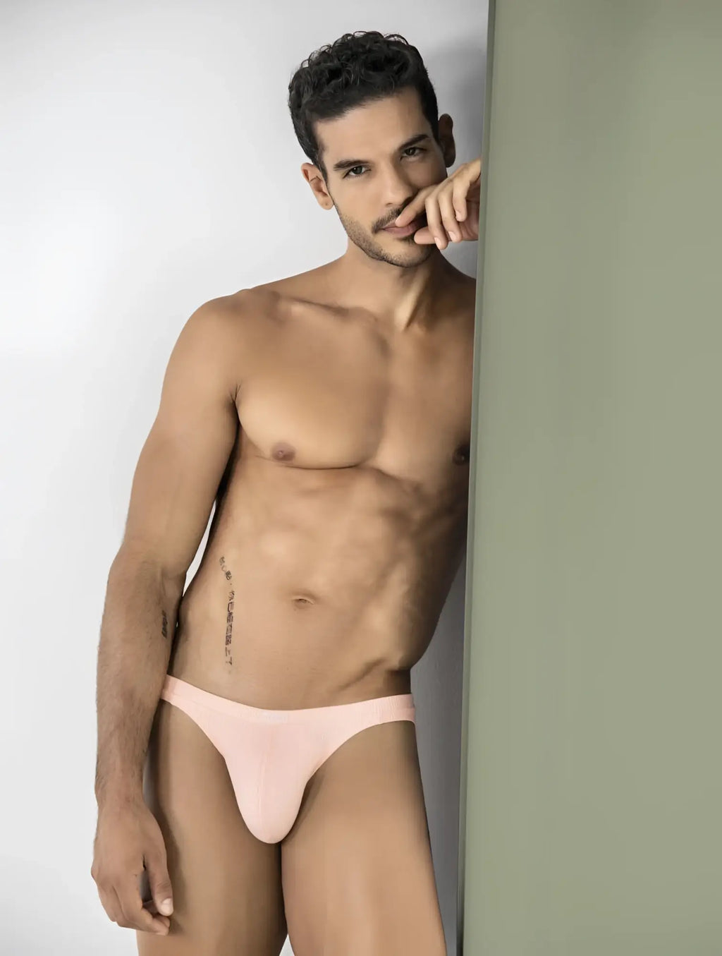 Clever 26017 Apolo bikini in vibrant orange, featuring a ribbed fabric design worn by a man leaning against a wall.