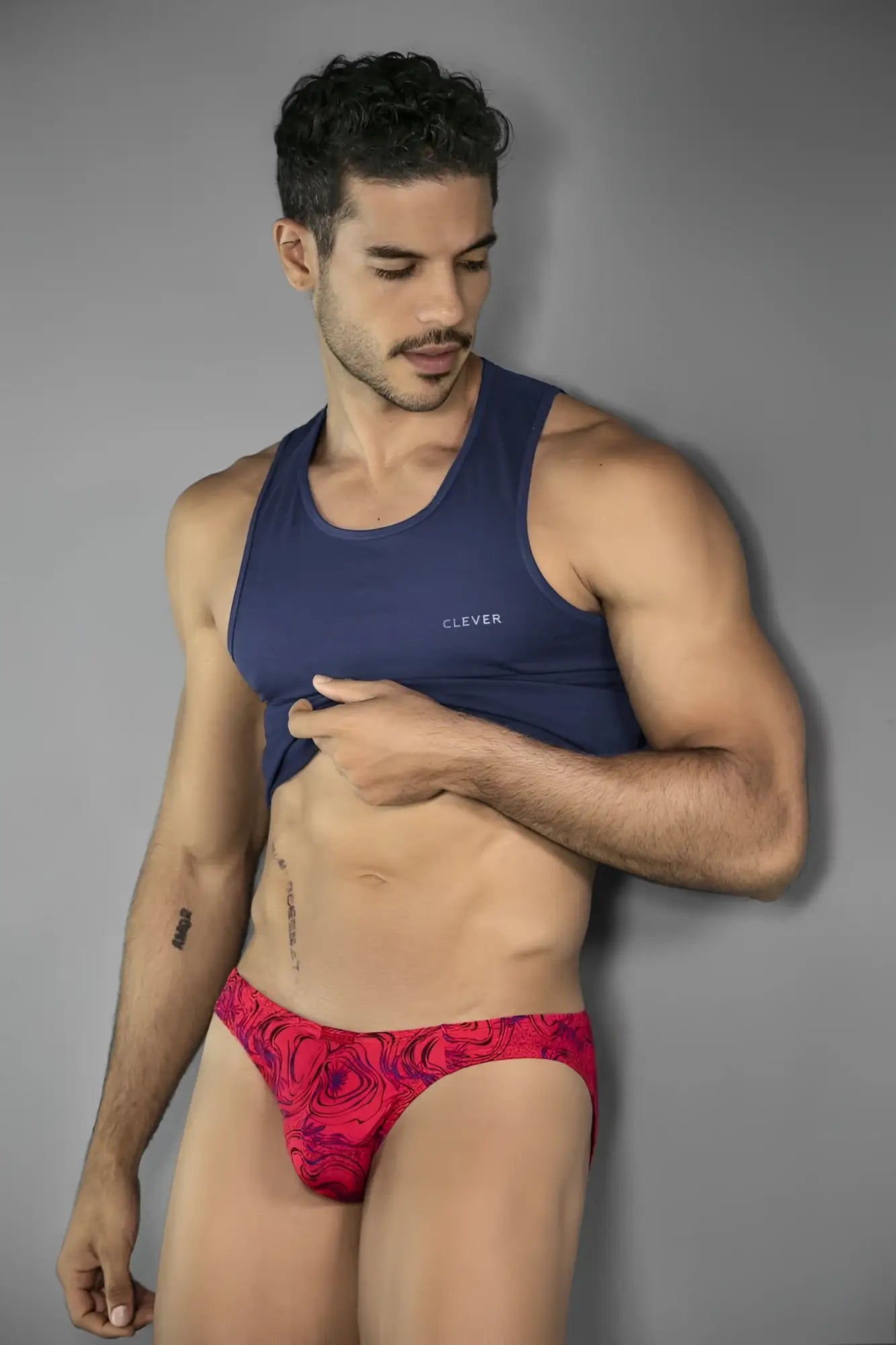 Model wearing a bold, vibrant red Clever 26028 Helion bikini brief with a modern swirling pattern.