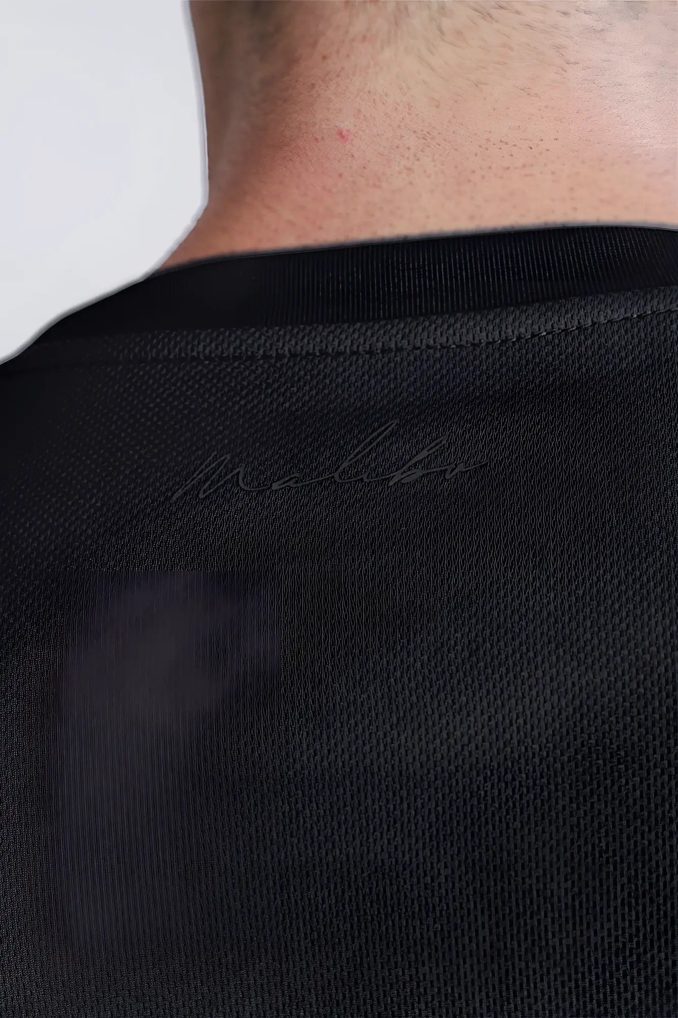 Back view of black cool-dry oversized relaxed crop top with textured fabric and subtle malibu logo embroidery