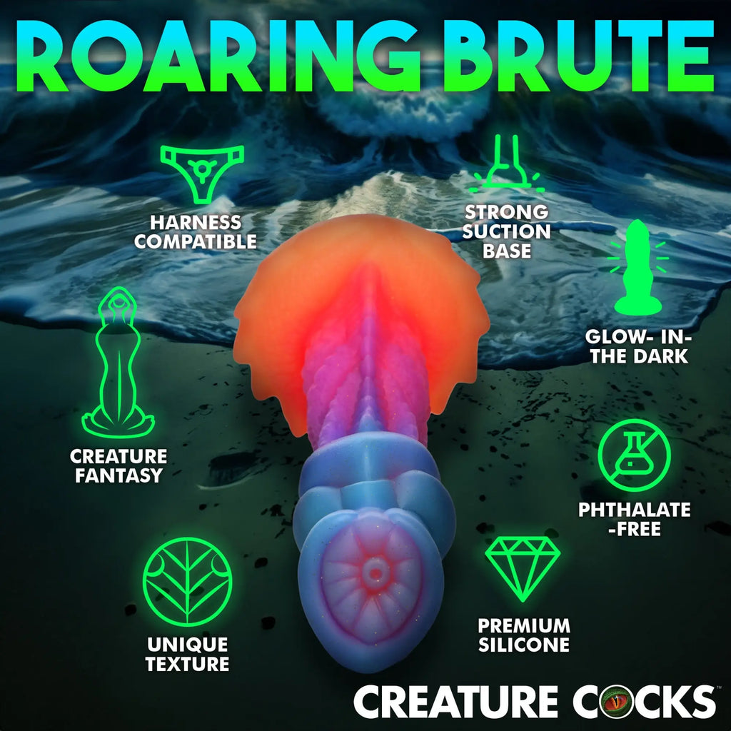 Creature Cocks Aqua-Cock glow-in-the-dark silicone dildo with textured blue and orange fantasy design against a beach.