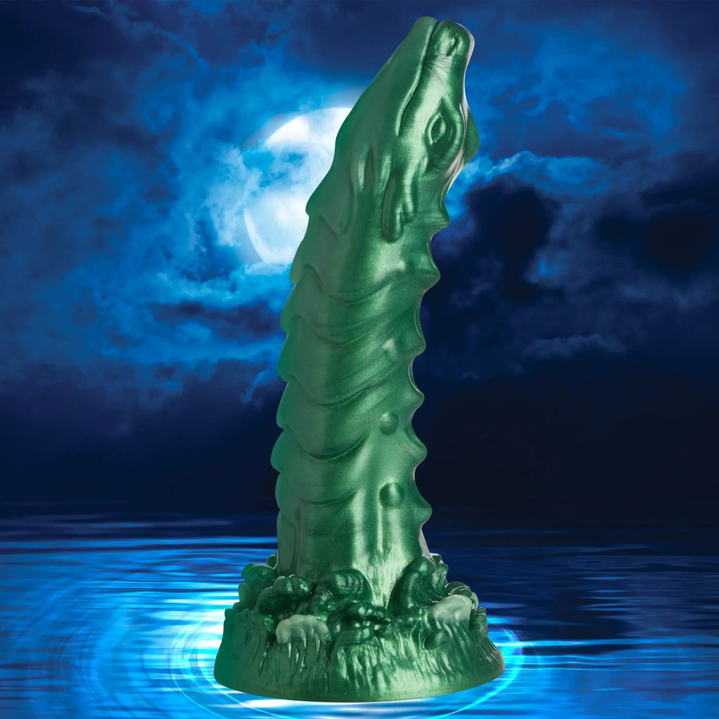 Creature Cocks Cockness Monster silicone dildo in metallic green with textured monster-like details against a night scene.