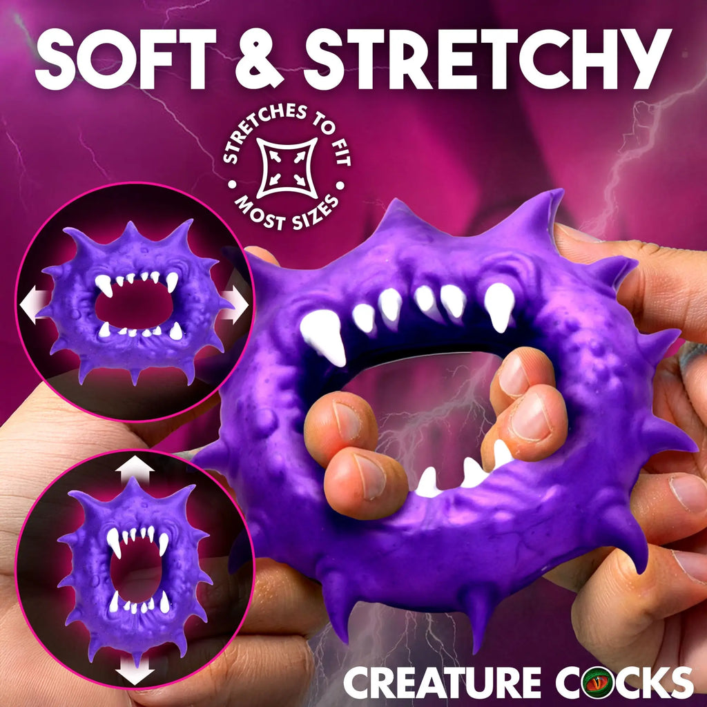 Purple Creature Cocks Constrictor silicone cock ring with monster spikes and teeth, being stretched by hands.