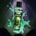 Creature Cocks Creature Cum green lubricant bottle, featuring a cartoon monster label, surrounded by green liquid splashes.