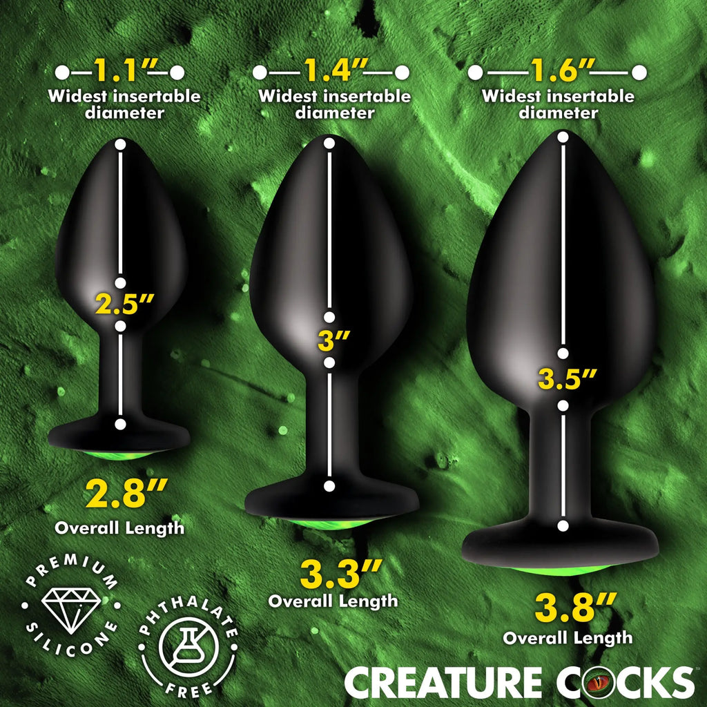Three black Creature Cocks Creature Eye silicone butt plugs of varying sizes shown with dimensions on a green background.