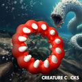 Creature Cocks Fangs: A red silicone cock ring with white tooth-like protrusions, set against a deep-sea creature backdrop.