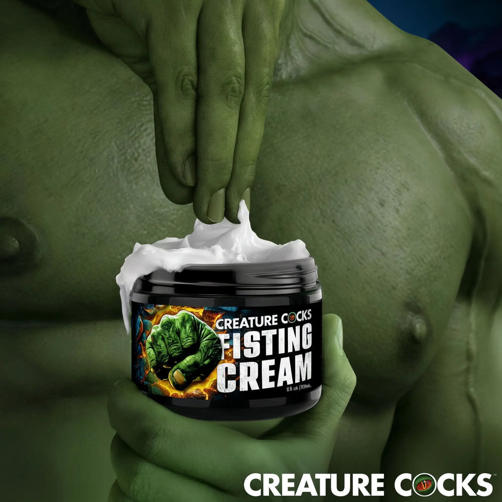 Creature Cocks Fisting Cream jar being scooped by a green, muscular hand, set against a muscular green background.