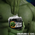 Creature Cocks Fisting Cream jar being scooped by a green, muscular hand, set against a muscular green background.