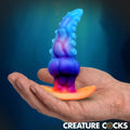 Creature Cocks Glowtopus silicone anal plug with tentacle texture, shifting from blue to orange in a palm-up hand.