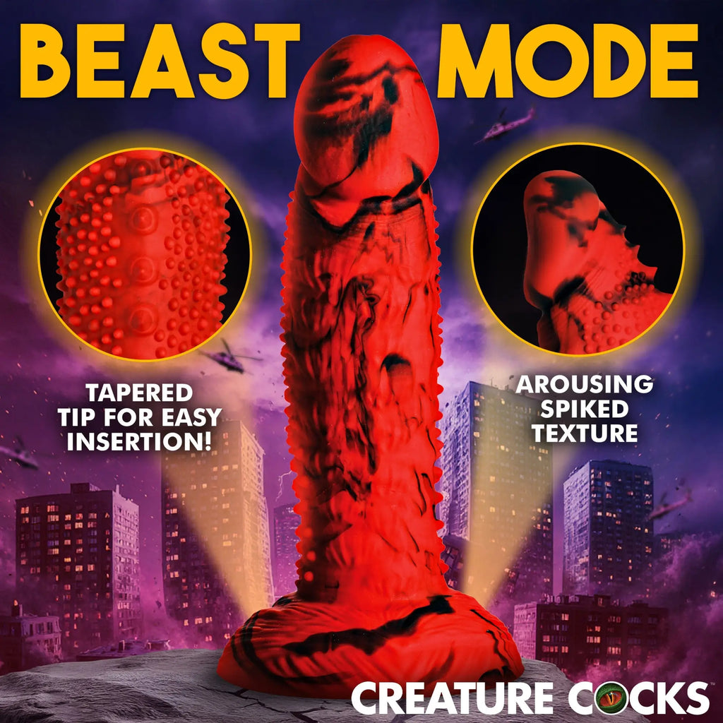 Creature Cocks Gojira red and black silicone dildo with spiked texture and tapered tip, shown against a city background.