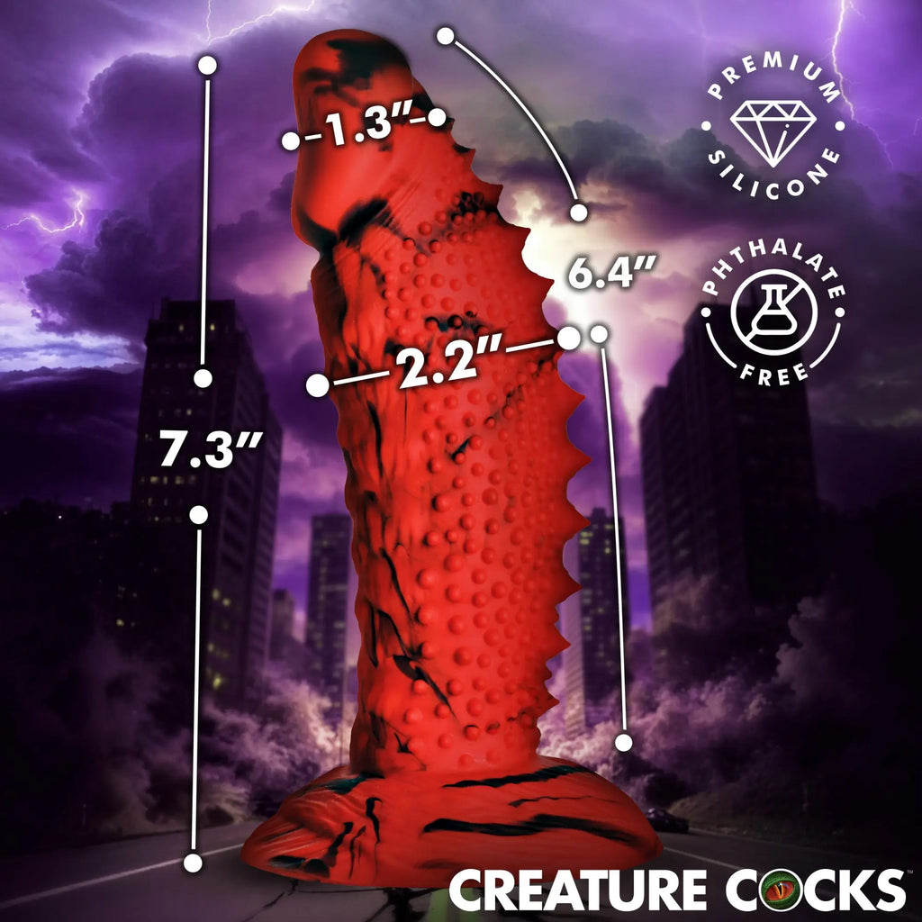 Creature Cocks Gojira red and black marbled silicone dildo with textured, fin-like detail against a stormy city background.
