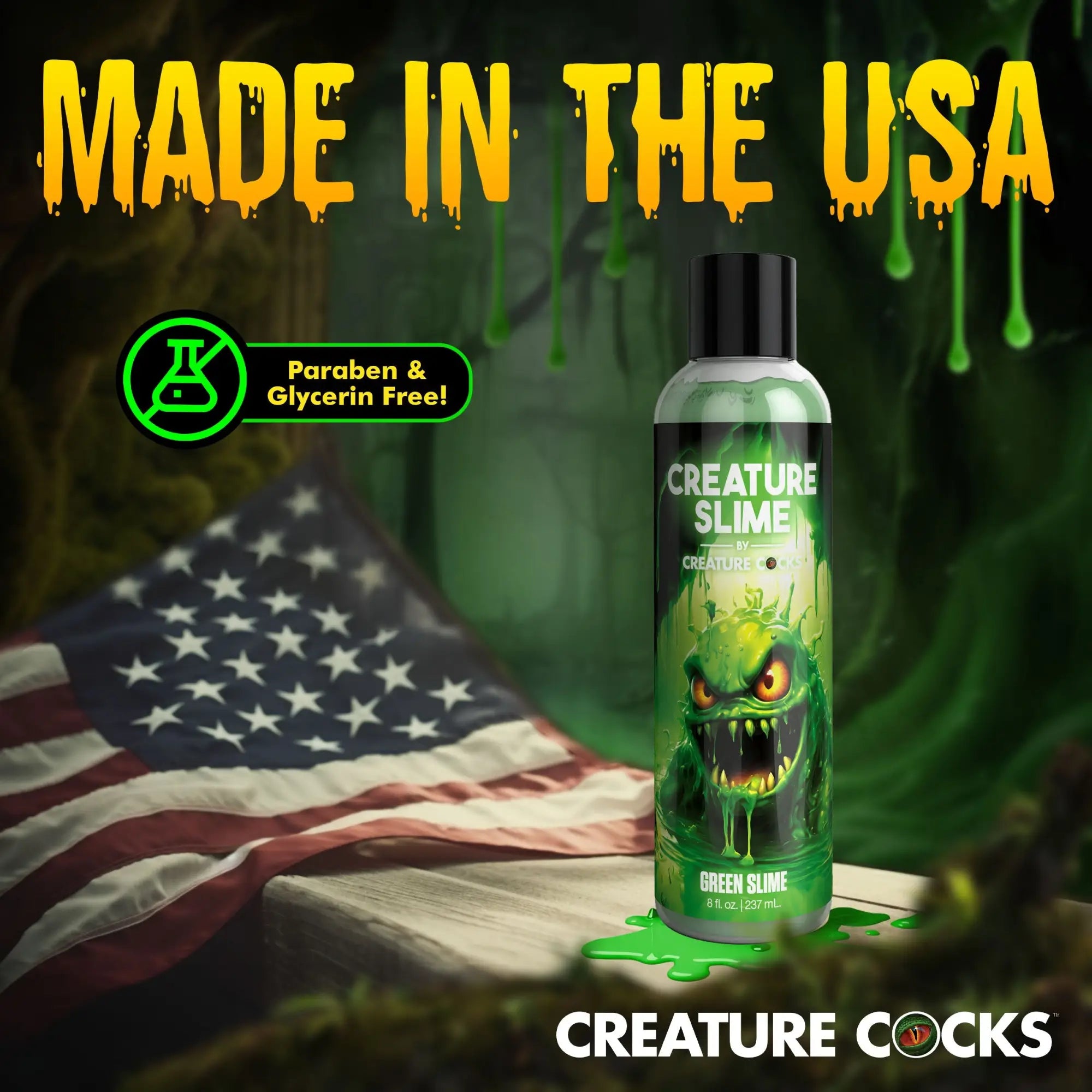Bottle of Creature Cocks Green Creature Slime lubricant with a monster graphic, next to a US flag on a wooden surface.