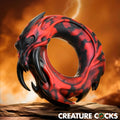 Creature Cocks Hell Fang silicone ring: a black and red, dragon-inspired textured ring displayed on a rock surface.