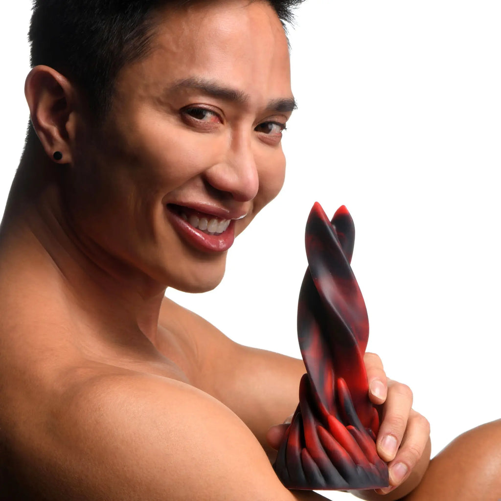 A smiling person holding a twisted, flame-colored red and black Creature Cocks Hell Kiss silicone dildo.