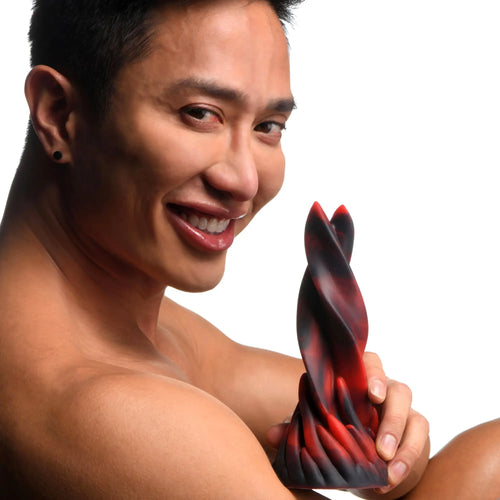A smiling person holding a twisted, flame-colored red and black Creature Cocks Hell Kiss silicone dildo.