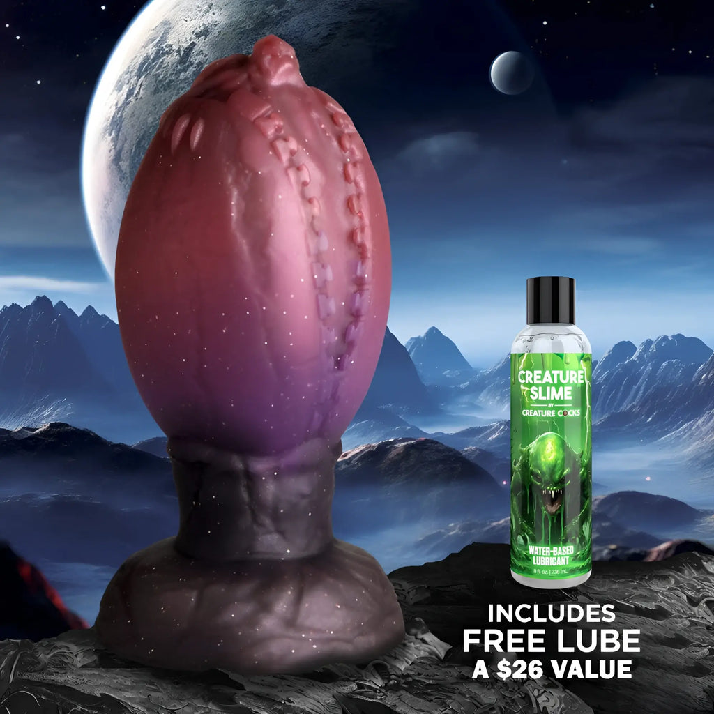Creature Cocks Large Dragon Hatch silicone egg in purple and black, with a bottle of lubricant against a space backdrop.