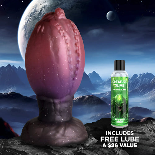Creature Cocks Large Dragon Hatch silicone egg in purple and black, with a bottle of lubricant against a space backdrop.