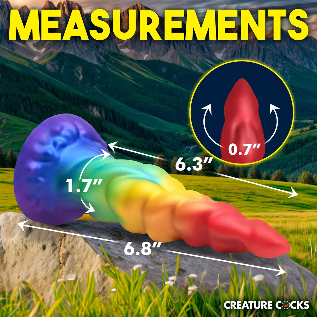 Creature Cocks Magic Rider unicorn dildo in rainbow gradient silicone with labeled measurements on a mountain background.