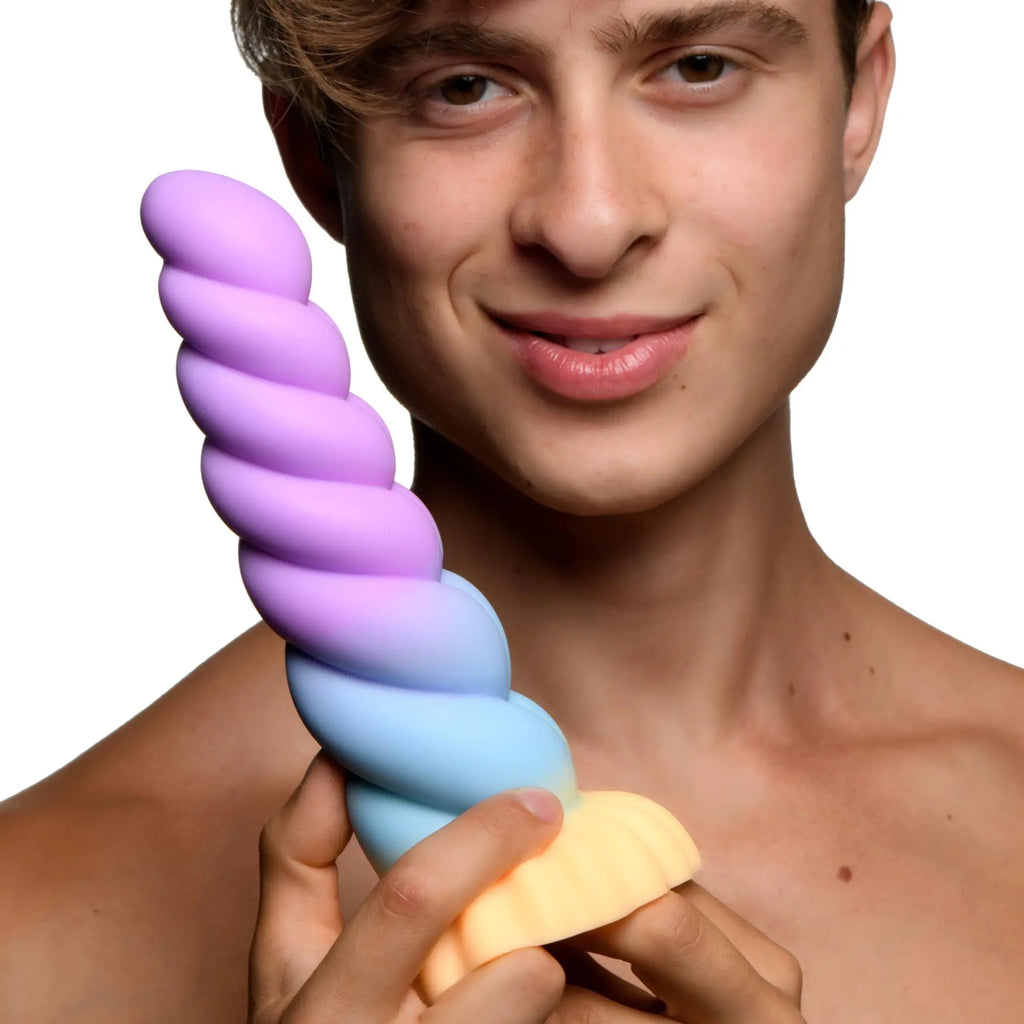 A person holding a spiraled, ombre-colored Creature Cocks Mystique silicone unicorn dildo fading from purple to peach.