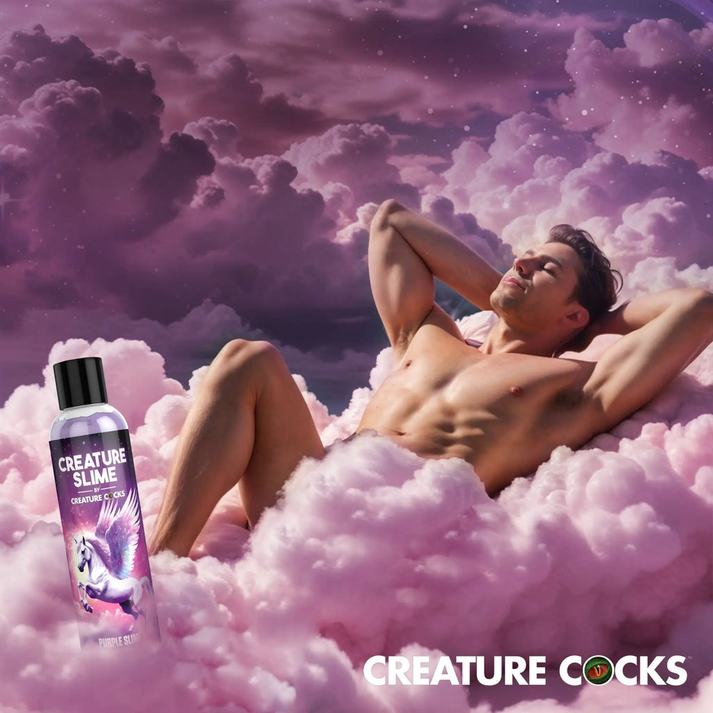 Bottle of Creature Cocks Purple Creature Slime lubricant next to a man relaxing in a dreamy, pink-cloud sky.