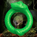 Creature Cocks Serpentine silicone cock ring in bright green, shaped like a coiled snake, against a jungle background.