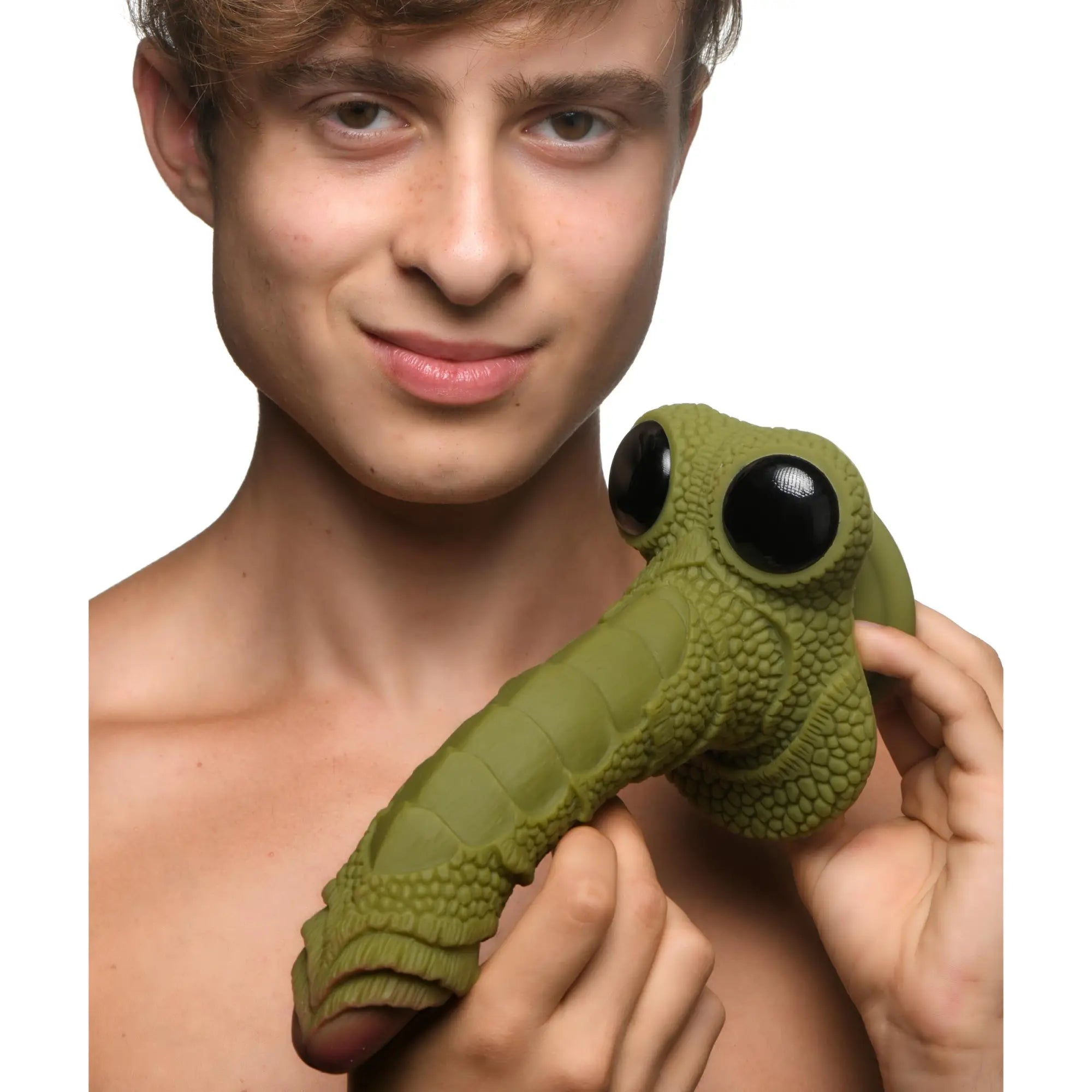 A man holds a green, scaly Creature Cocks Swamp Monster silicone dildo featuring large, black, bug-like eyes.